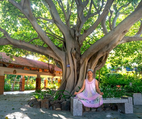 Person smiling and stretching outdoors in a green park at sunrise.